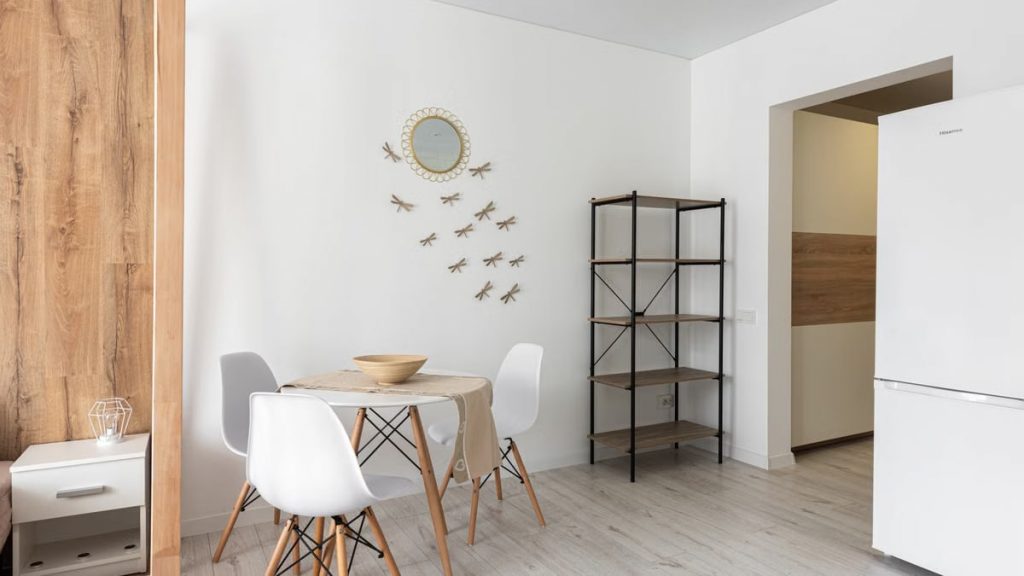 Contemporary dining room with table and chairs against decorative dragonflies and mirror on wall at home with refrigerator and shelves