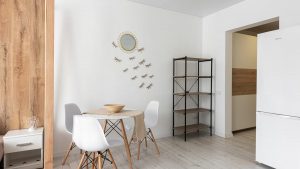 Contemporary dining room with table and chairs against decorative dragonflies and mirror on wall at home with refrigerator and shelves
